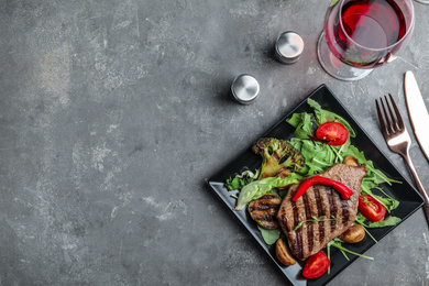 Photo of Delicious beef steak served on grey table, flat lay. Space for text