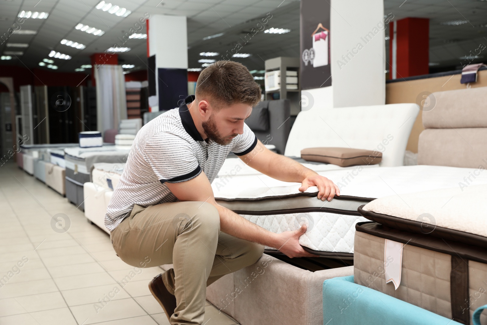 Photo of Young man choosing new orthopedic mattress in store