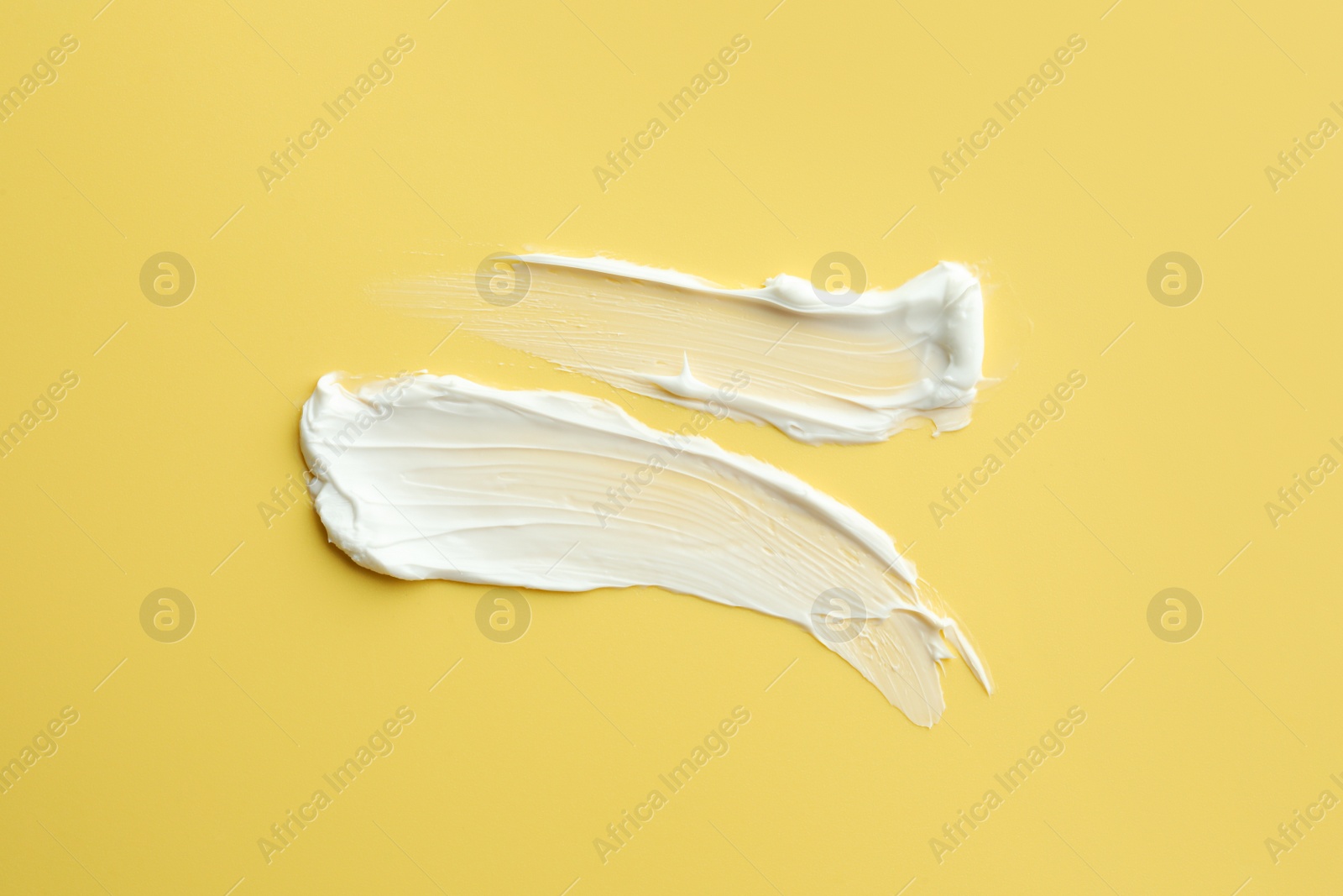 Photo of Samples of face cream on yellow background, top view