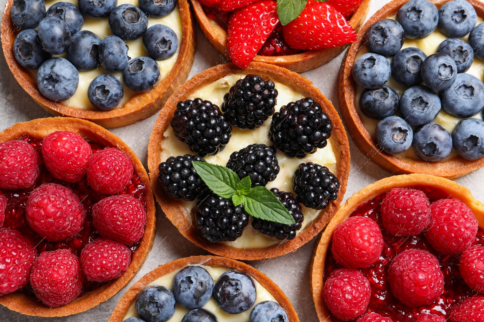 Photo of Tartlets with different fresh berries on light table, flat lay. Delicious dessert
