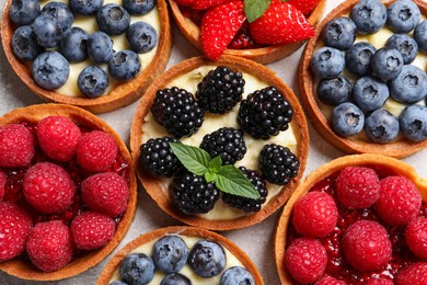 Tartlets with different fresh berries on light table, flat lay. Delicious dessert