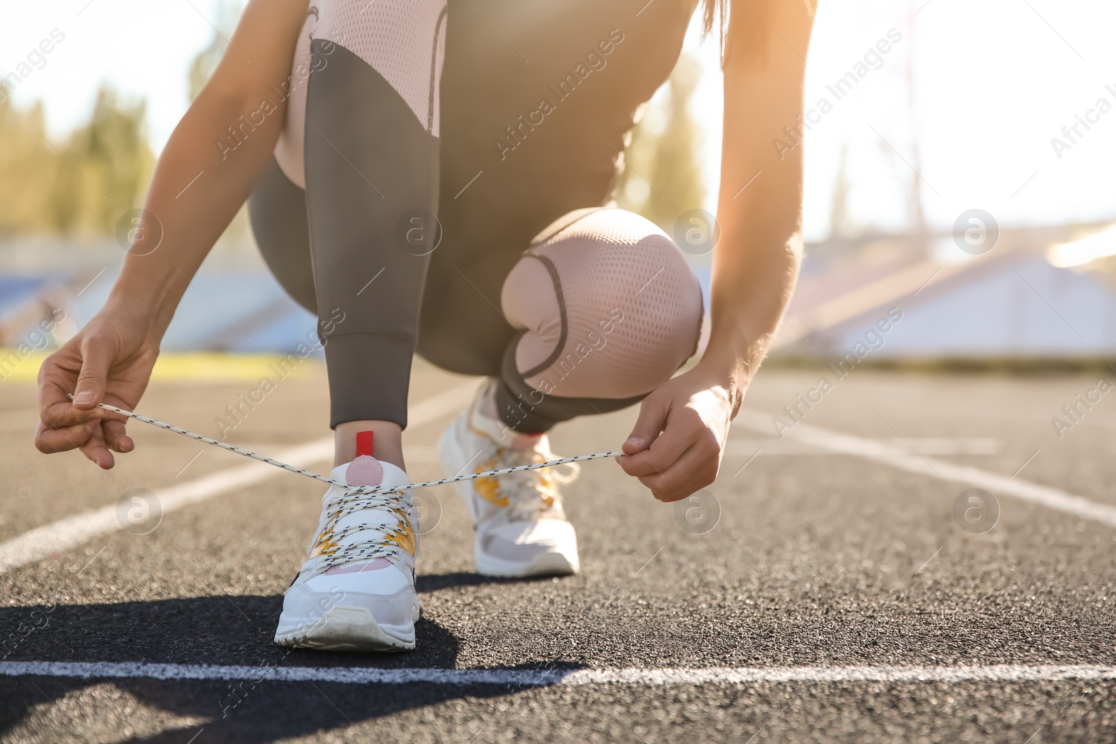 Photo of Sporty woman tying shoelaces before running at stadium on sunny morning