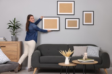 Woman hanging picture frame on gray wall at home