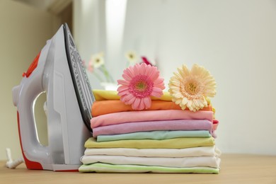 Photo of Stack of clean clothes, modern iron and flowers on wooden table