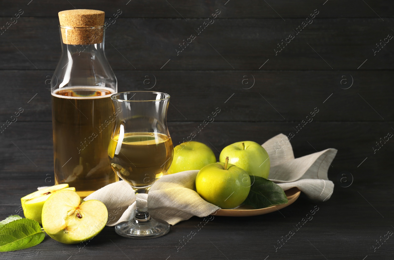 Photo of Delicious cider and apples with green leaves on black wooden table