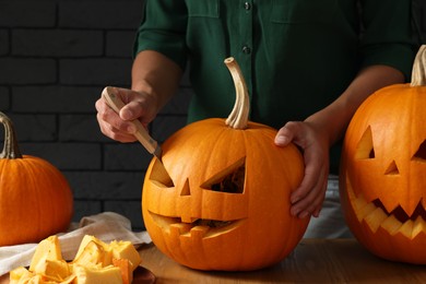 Photo of Woman carving pumpkin at wooden table, closeup. Halloween celebration