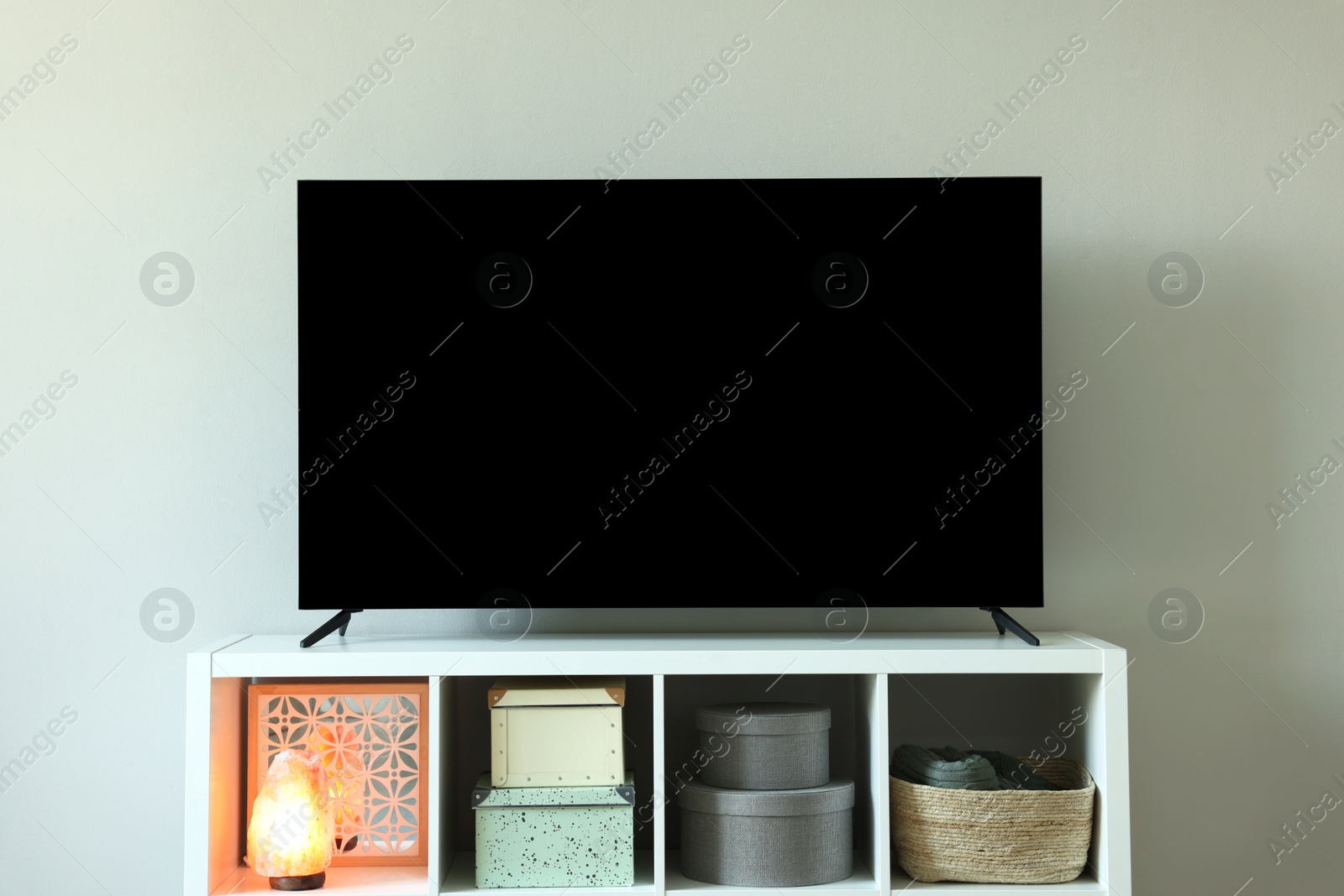 Photo of Modern TV and lamp on cabinet near white wall indoors. Interior design