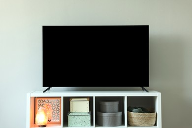 Modern TV and lamp on cabinet near white wall indoors. Interior design
