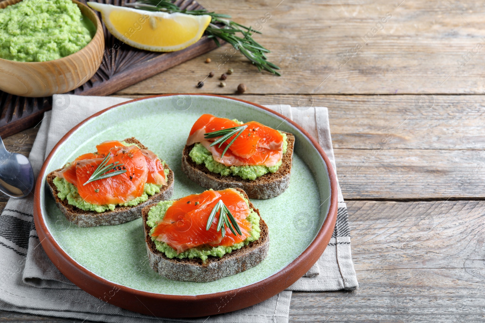 Photo of Delicious sandwiches with salmon, avocado and rosemary on wooden table. Space for text