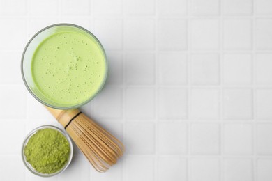 Glass of tasty matcha smoothie, powder and bamboo whisk on white tiled table, flat lay. Space for text