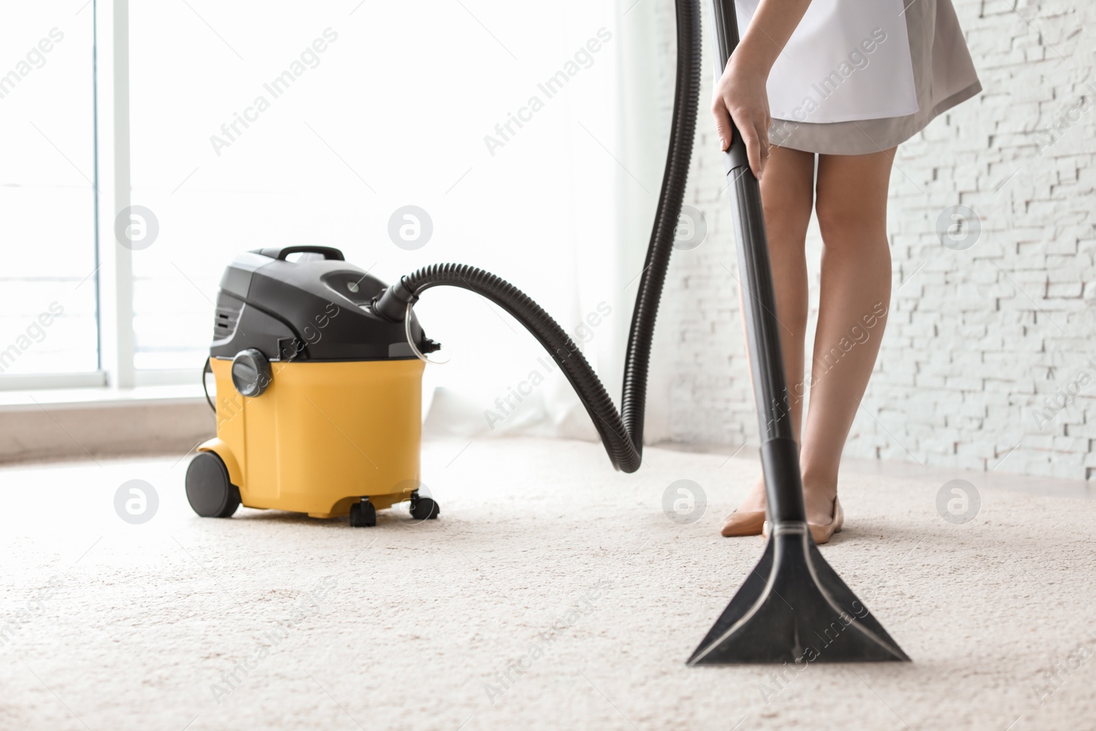 Photo of Chambermaid cleaning carpet with vacuum  indoors