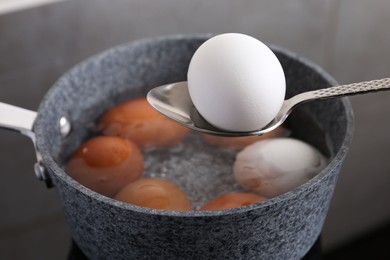 Photo of Spoon with boiled egg above saucepan on electric stove, closeup