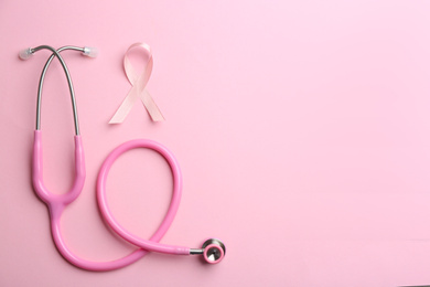 Pink ribbon as breast cancer awareness symbol and stethoscope on color background, flat lay. Space for text