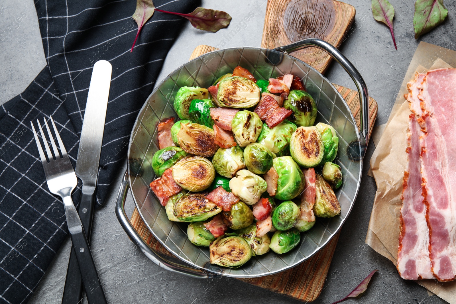 Photo of Delicious Brussels sprouts with bacon served on grey table, flat lay