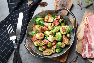 Delicious Brussels sprouts with bacon served on grey table, flat lay