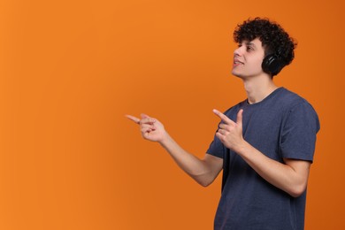 Photo of Handsome young man in headphones pointing at something on orange background. Space for text