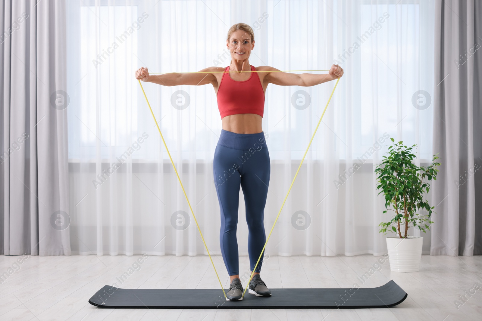 Photo of Fit woman doing exercise with fitness elastic band on mat at home