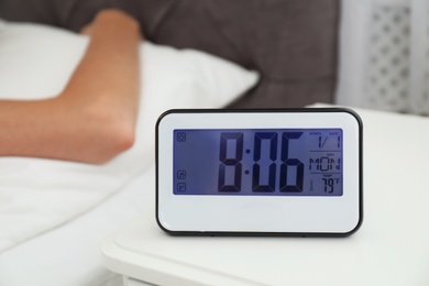Photo of Digital alarm clock and blurred woman on background. Time of day