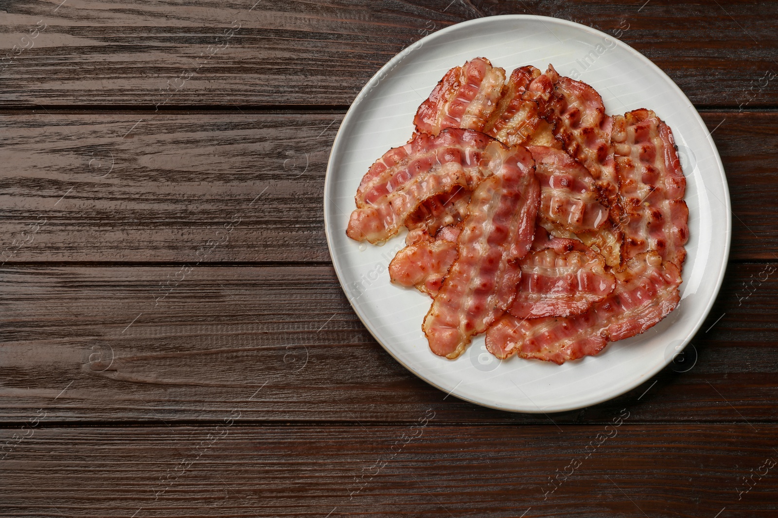 Photo of Plate with fried bacon slices on wooden table, top view. Space for text