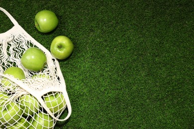 Photo of Ripe green apples and net bag on grass, flat lay. Space for text