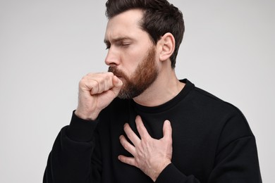 Sick man coughing on light grey background. Cold symptoms