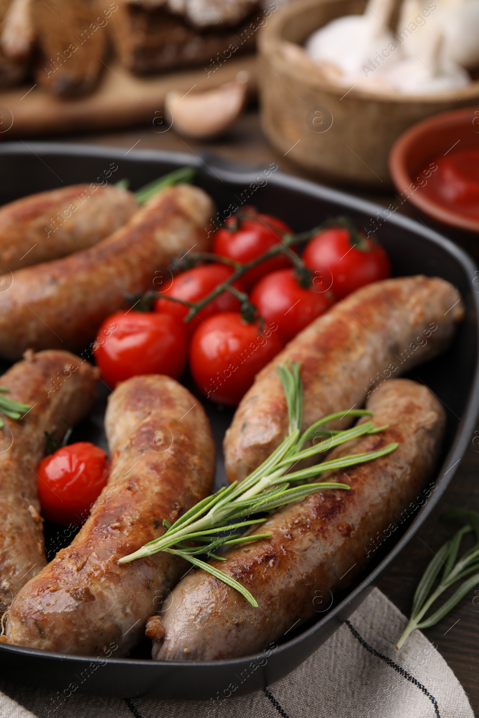 Photo of Grill pan with tasty homemade sausages, rosemary and tomatoes on table, closeup