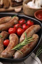 Photo of Grill pan with tasty homemade sausages, rosemary and tomatoes on table, closeup