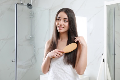 Photo of Beautiful young woman with hair brush in bathroom