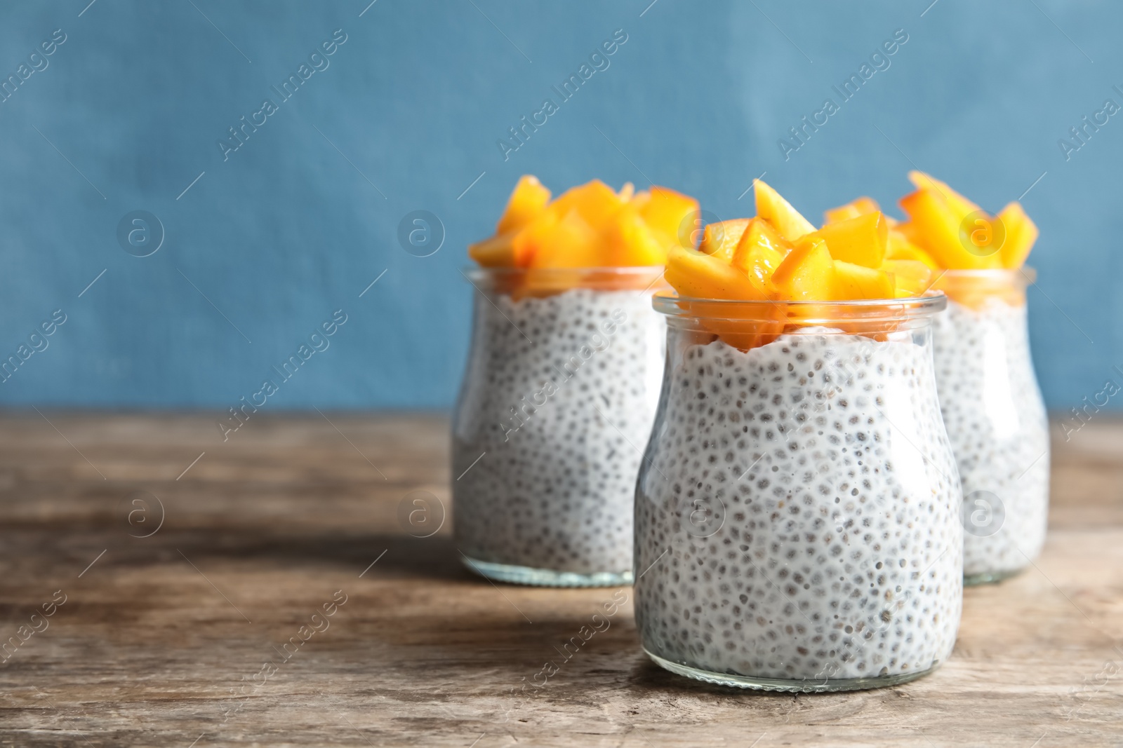 Photo of Jars of tasty chia seed pudding with persimmon on table, space for text