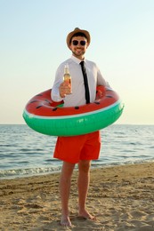 Photo of Happy man with inflatable ring and beer on beach. Business trip