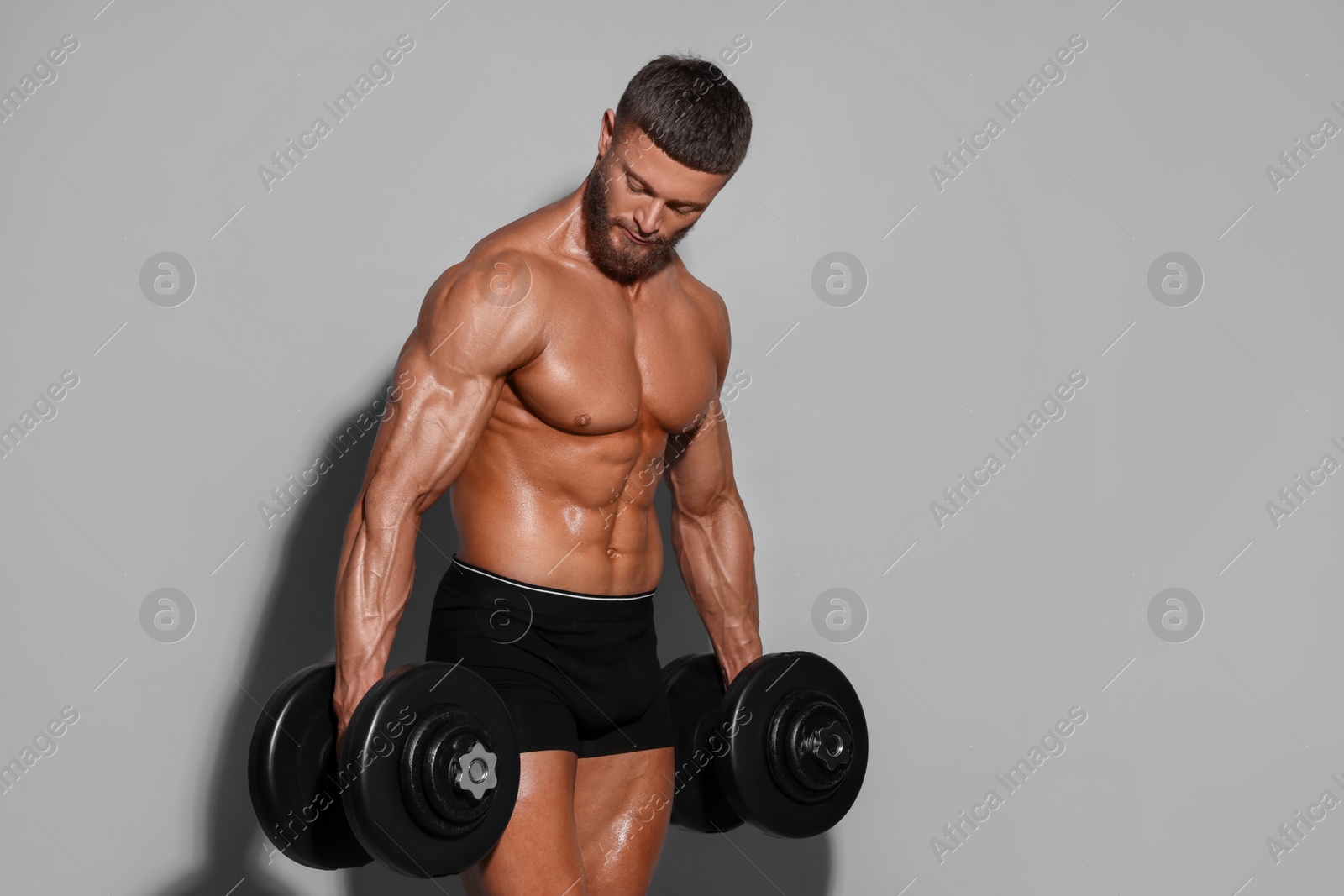 Photo of Young bodybuilder exercising with dumbbells on light grey background, space for text