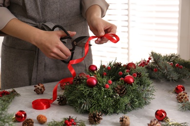 Florist making beautiful Christmas wreath at grey table indoors, closeup