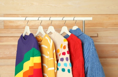 Collection of warm sweaters hanging on rack against wooden background