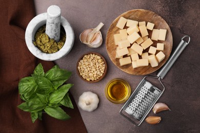 Photo of Tasty pesto sauce and ingredients on brown textured table, flat lay