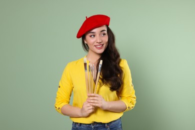 Photo of Woman with paintbrushes on pale green background. Young artist