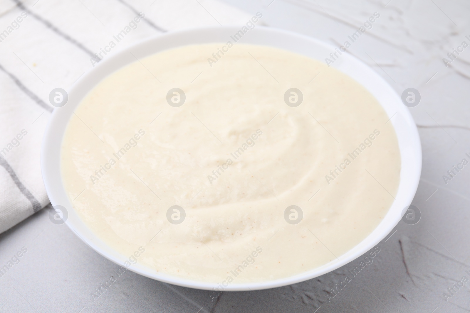 Photo of Delicious semolina pudding in bowl on white textured table, closeup