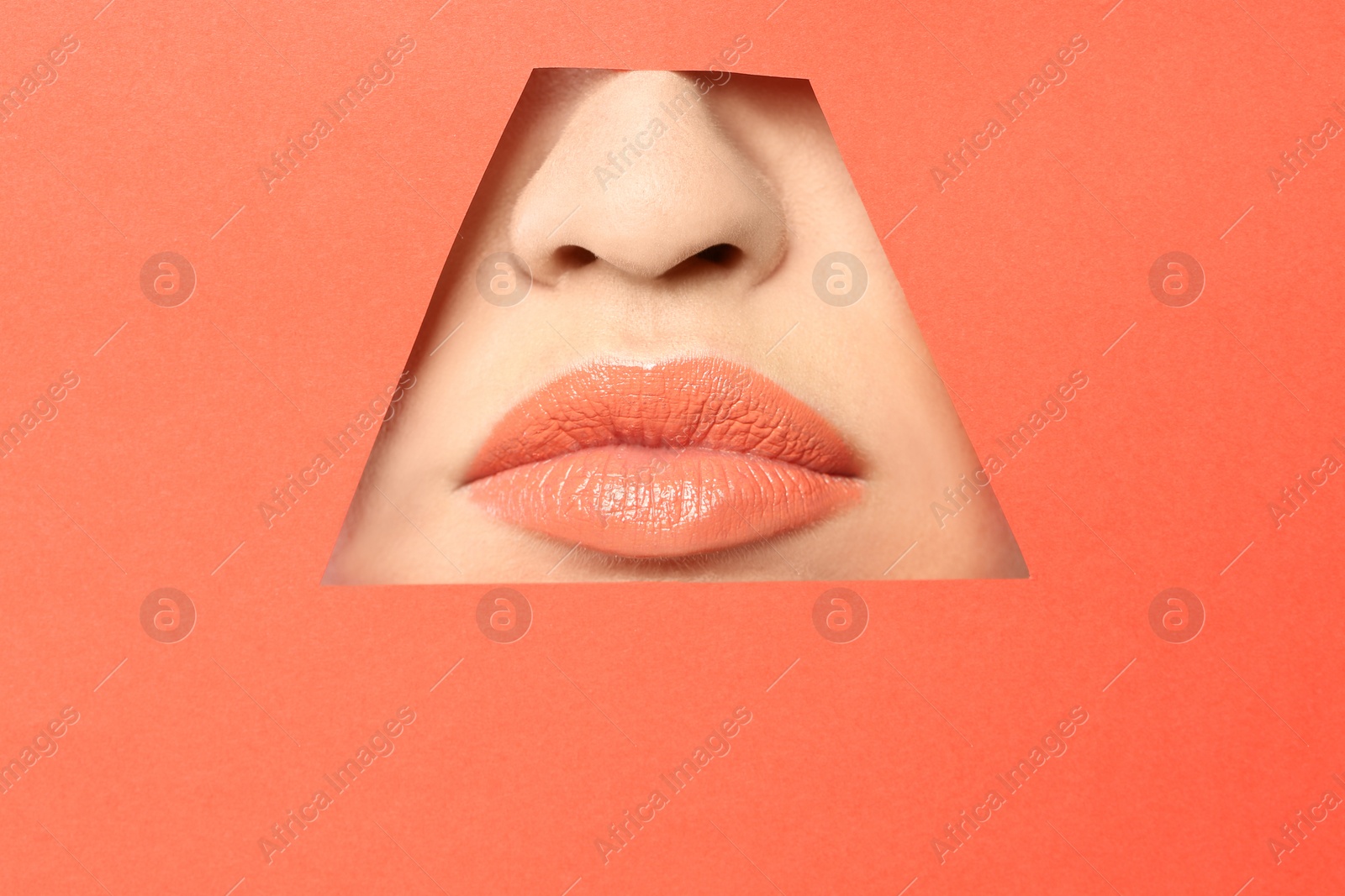 Photo of Lips of young woman with beautiful lipstick visible through hole in color paper