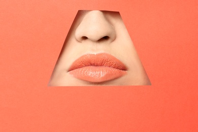 Lips of young woman with beautiful lipstick visible through hole in color paper