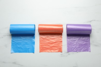 Photo of Rolls of different color garbage bags on white marble table, flat lay