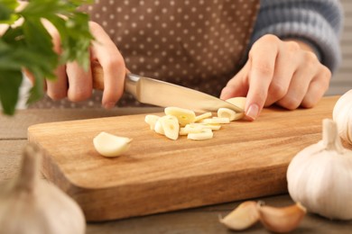 Photo of Woman cutting fresh garlic at table, closeup