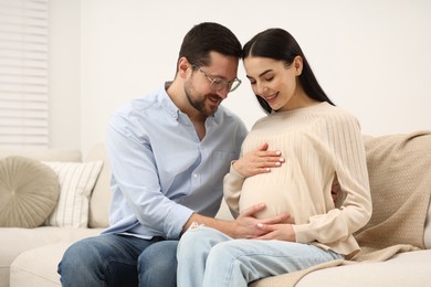 Photo of Happy pregnant woman with her husband on sofa at home