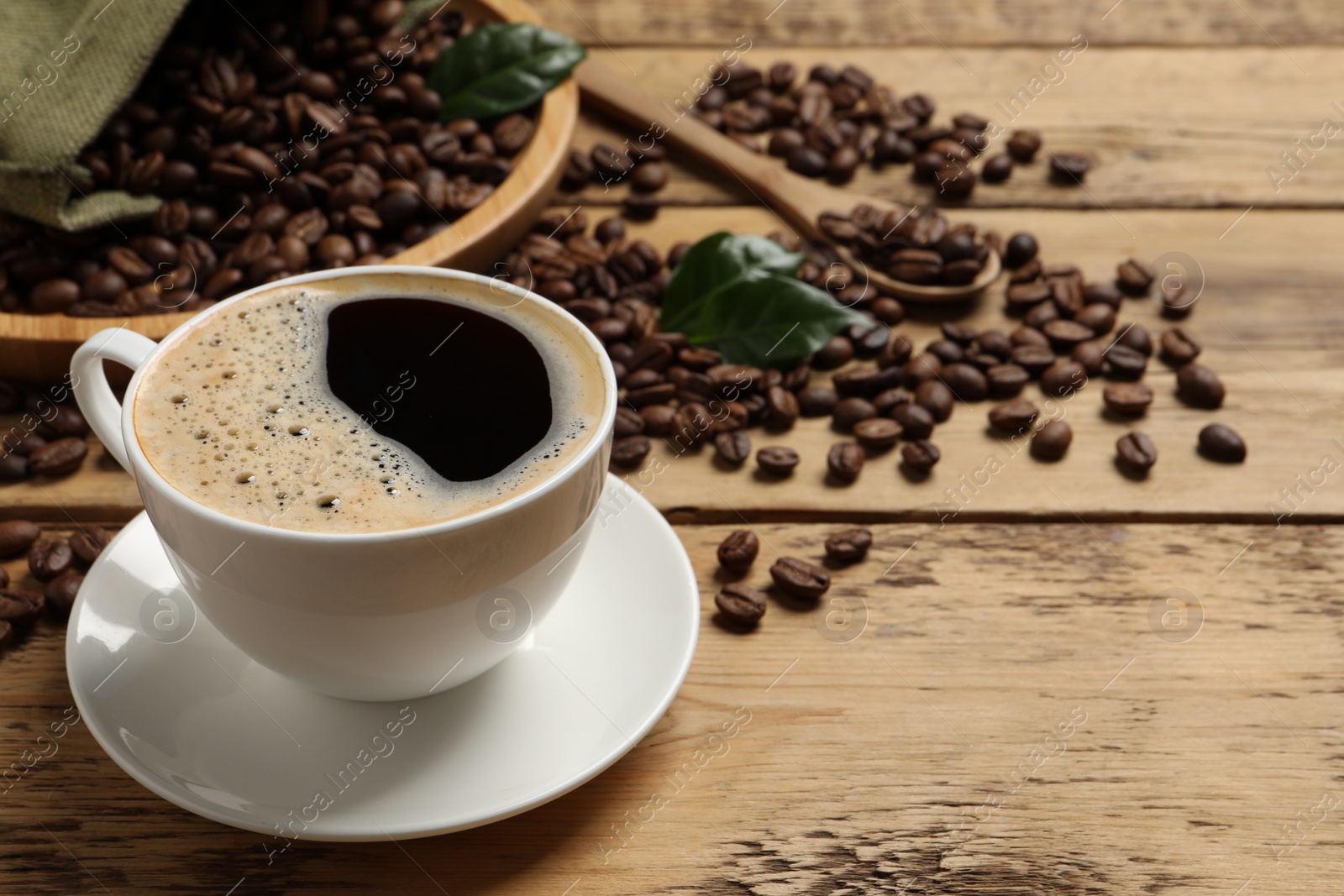 Photo of Cup of aromatic hot coffee and beans on wooden table, space for text