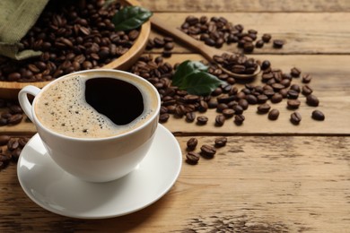 Cup of aromatic hot coffee and beans on wooden table, space for text