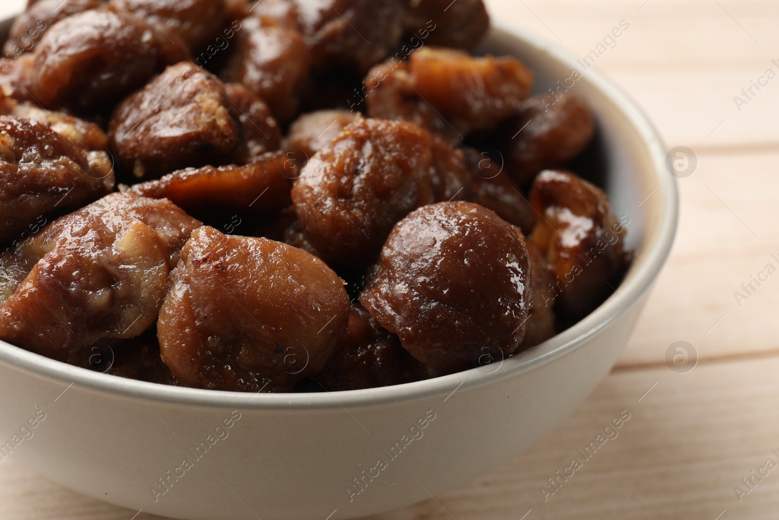 Photo of Roasted edible sweet chestnuts in bowl on light wooden table, closeup