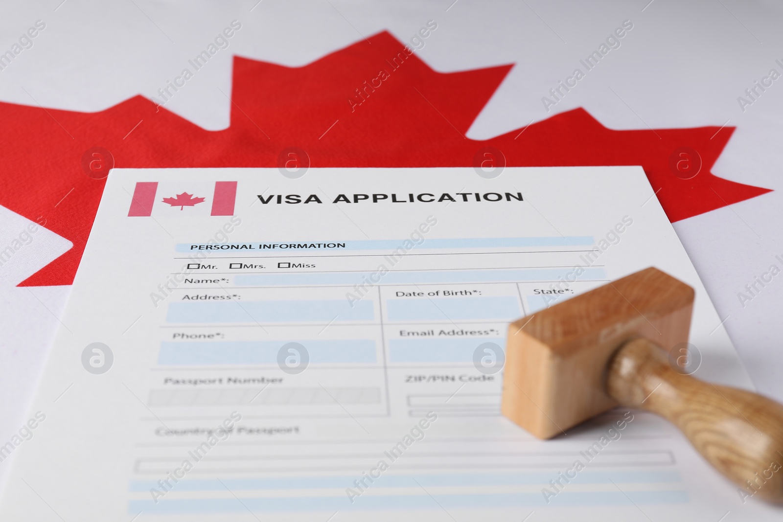 Photo of Immigration to Canada. Visa application form and wooden stamp on flag, closeup