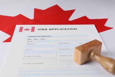 Immigration to Canada. Visa application form and wooden stamp on flag, closeup