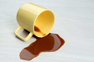 Photo of Overturned cup and spilled coffee on white wooden table