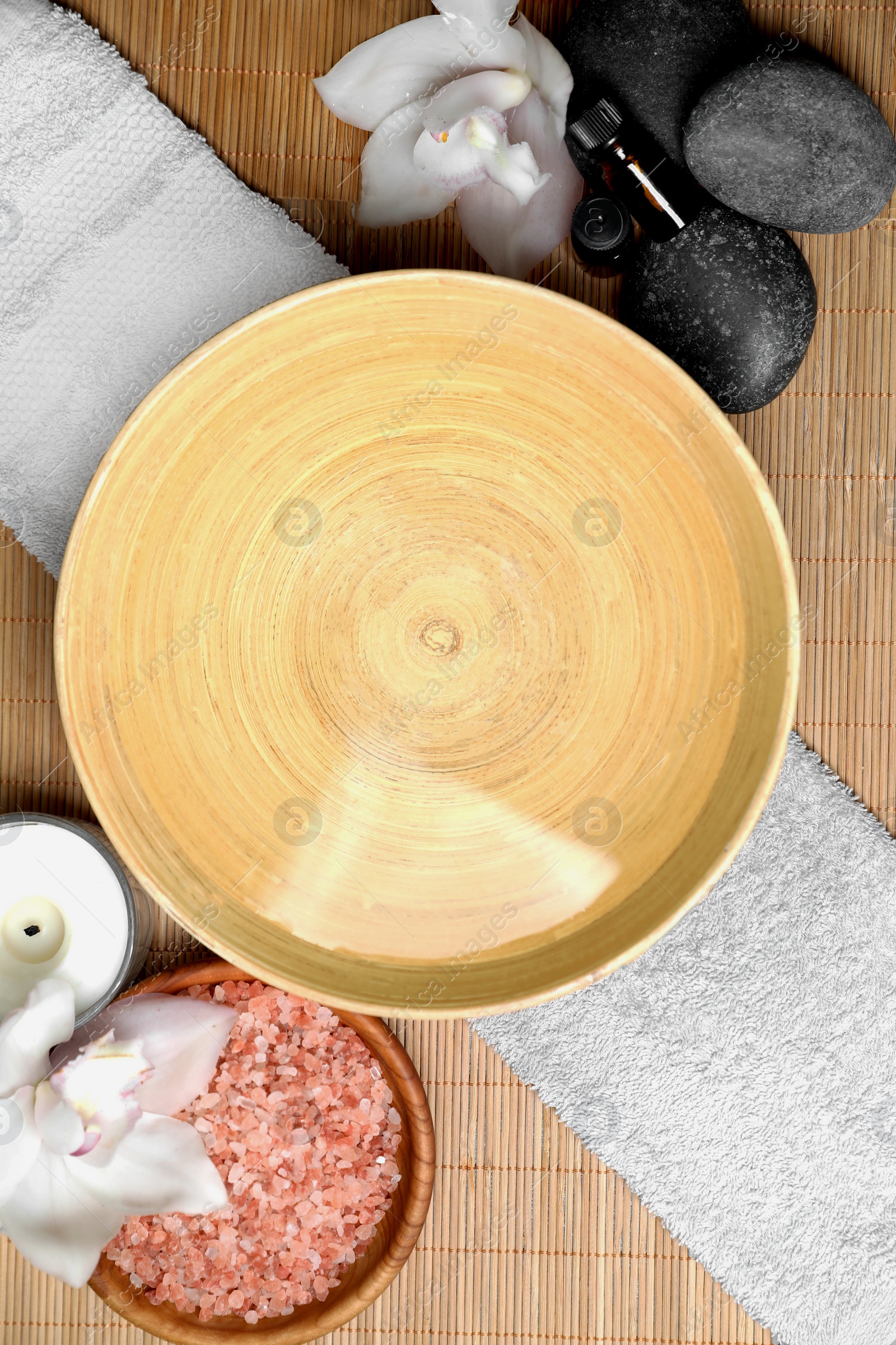 Photo of Bowl with water and beautiful flowers on bamboo mat, flat lay. Spa treatment