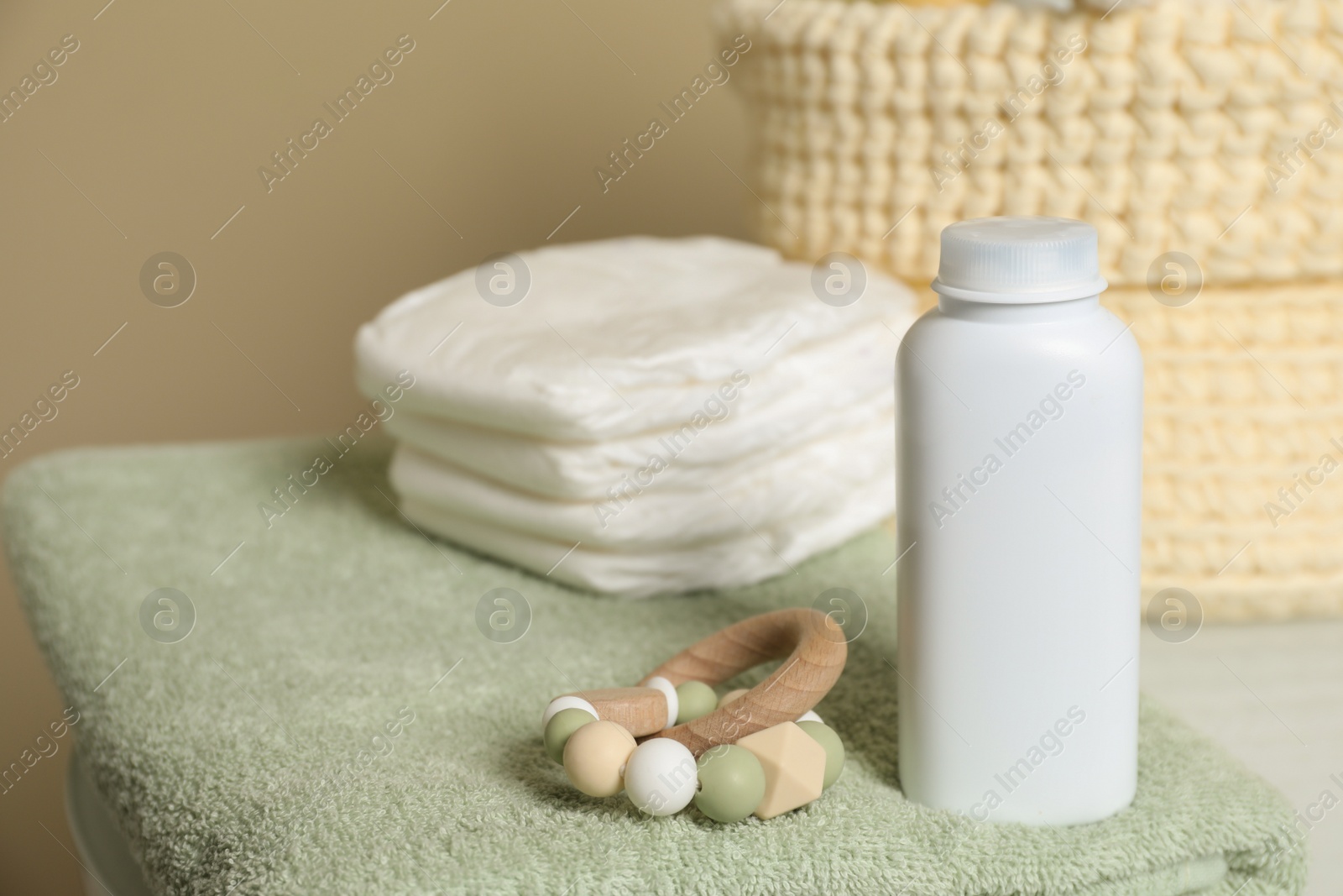 Photo of Bottle of dusting powder, wooden toy, soft towel and diapers on beige background, space for text. Baby cosmetic product