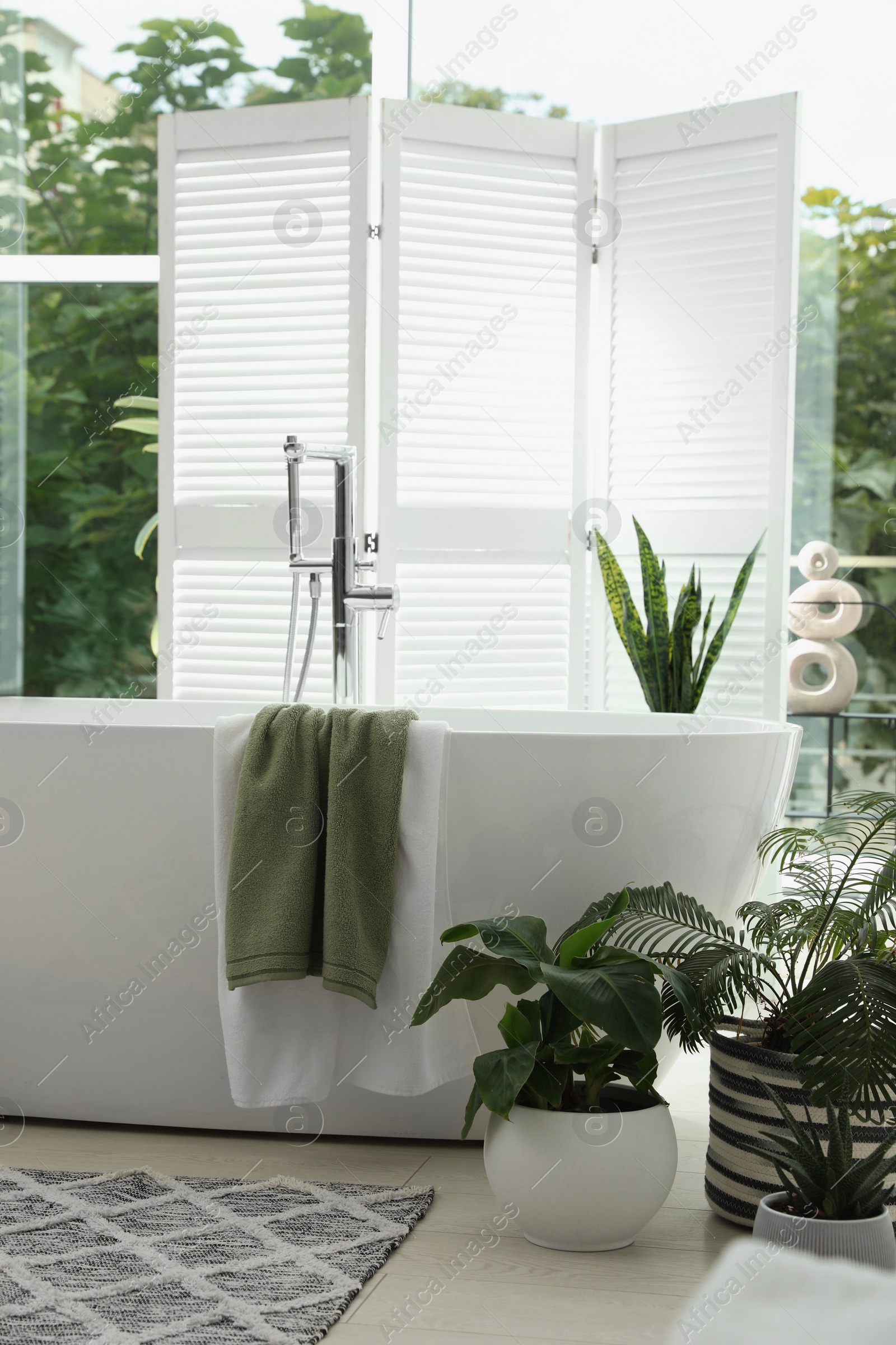 Photo of Stylish bathroom interior with modern tub, window and beautiful houseplants. Home design